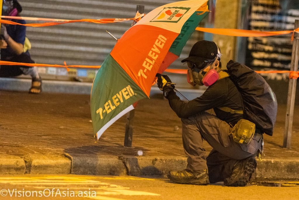 A protester takes cover under an umbrella to approach a police station