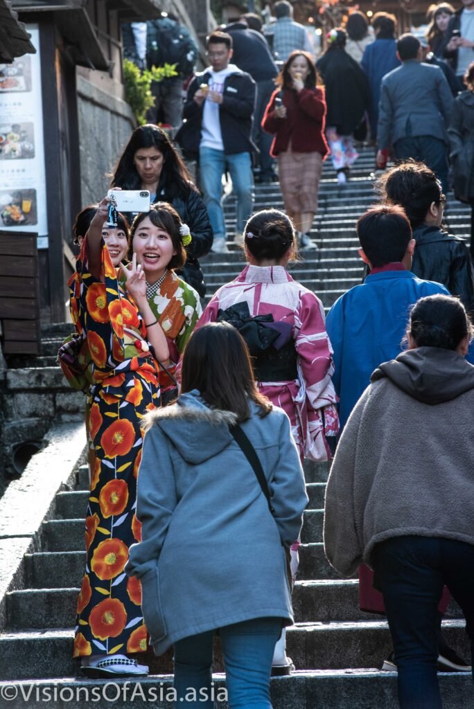 Two young ladies in kimono take a selfie on stairs in Kyoto