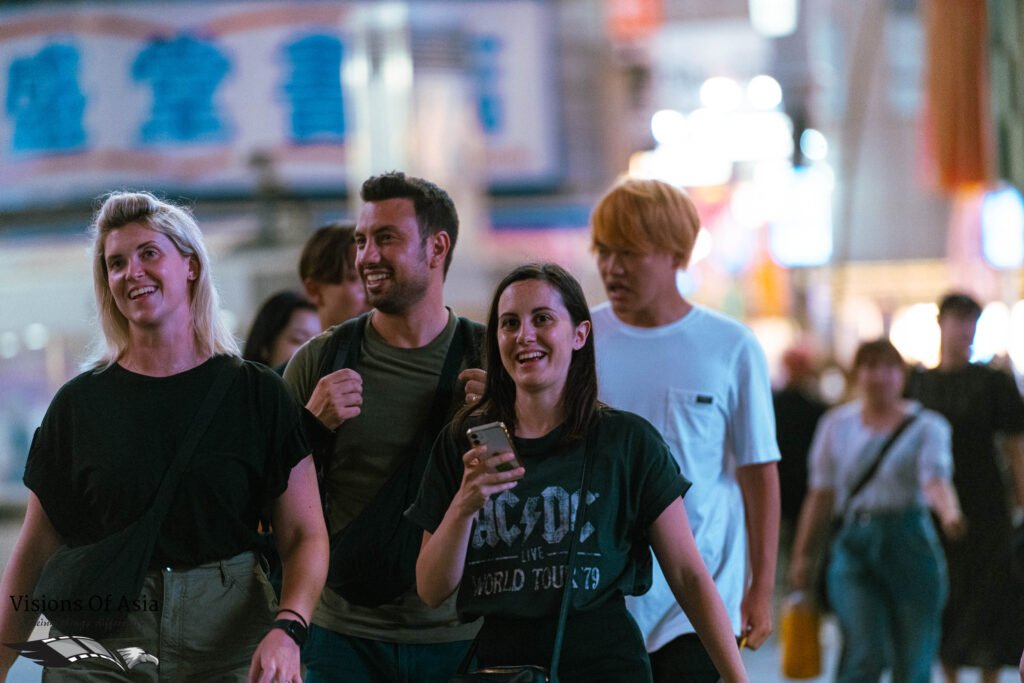 Smiling Western tourists walk across the Shibuya scrambled crossing.